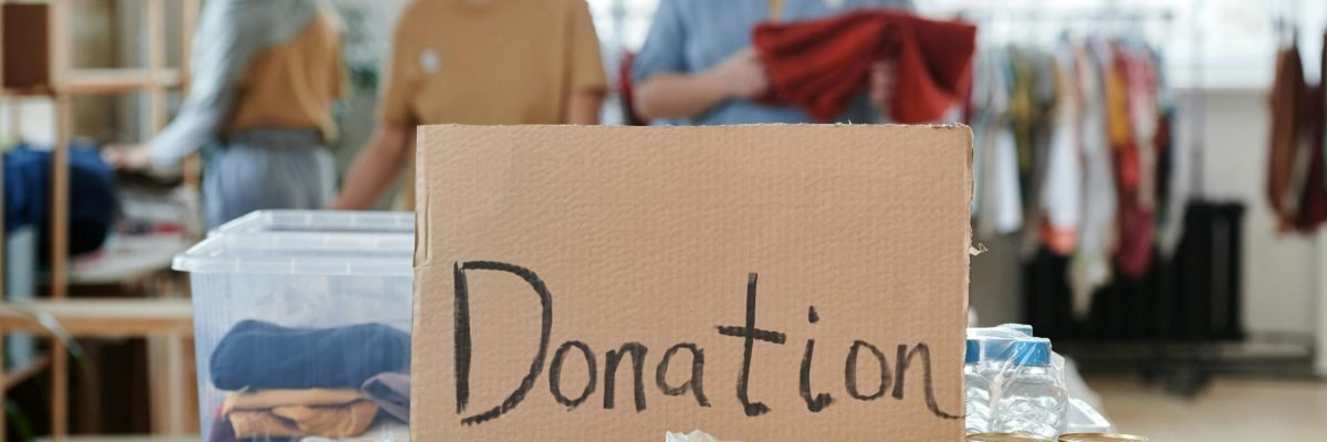 Volunteers sort clothes and food in a donation center. Cardboard sign reads 'Donation.'